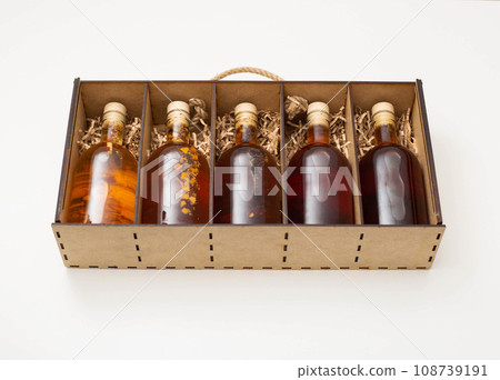 gift set of bottles with brown alcohol whiskey and brandy. Homemade herbal tincture in a wooden box on a white background. gift set of bottles with brown alcohol whiskey and brandy. Homemade herbal tincture in a wooden box on a white background. 108739191