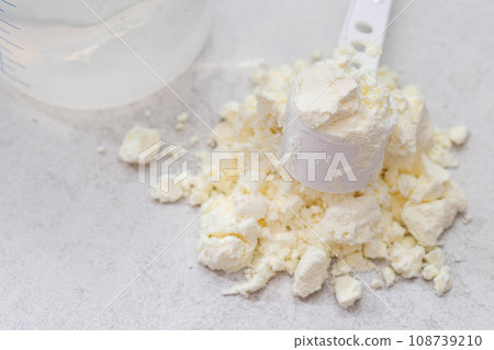A baby feeding bottle and a measuring spoon with a handful of dry baby formula for preparing milk for the baby. Useful and healthy food, close-up A baby feeding bottle and a measuring spoon with a handful of dry baby formula for preparing milk for the baby. Useful and healthy food, close-up 108739210