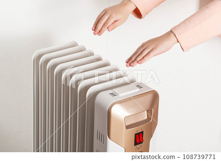 Children's hands on the background of an oil electric heater on a white background. Concept for turning on heating in apartments, temperature in the house. Children's hands on the background of an oil electric heater on a white background. Concept for turning on heating in apartments, temperature in the house. 108739771