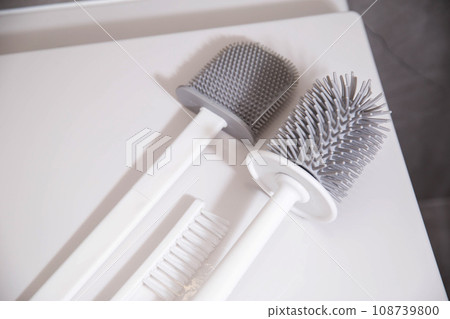 Silicone brushes for cleaning the toilet lie on the lid of the wall-hung toilet. The concept of care and cleaning the toilet from dirt and bacteria. Gray stoneware tiles on the walls. Silicone brushes for cleaning the toilet lie on the lid of the wall-hung toilet. The concept of care and cleaning the toilet from dirt and bacteria. Gray stoneware tiles on the walls. 108739800