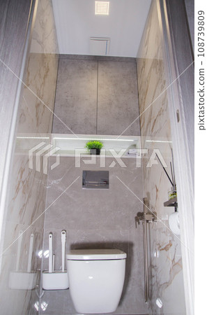 View of the interior of a modern bathroom renovation with a hanging toilet bowl, a hygienic shower and porcelain stoneware tiles on the walls. Niche with diode tape View of the interior of a modern bathroom renovation with a hanging toilet bowl, a hygienic shower and porcelain stoneware tiles on the walls. Niche with diode tape 108739809