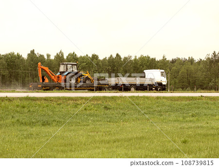 A semi-trailer truck transports an oversized tractor on the road. Transportation of oversized cargo by highway. Copy space for text, industry A semi-trailer truck transports an oversized tractor on the road. Transportation of oversized cargo by highway. Copy space for text, industry 108739815