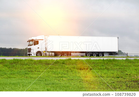 A beautiful new white semi-trailer truck transports cargo along the road in summer. Concept of commercial cargo transportation, logistics services. Trucking business. Side view. Copy space for text A beautiful new white semi-trailer truck transports cargo along the road in summer. Concept of commercial cargo transportation, logistics services. Trucking business. Side view. Copy space for text 108739820