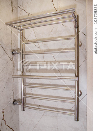 Modern stainless steel water heated towel rail hanging on the wall in the bathroom, close-up 108739828