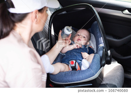 A mother feeds her baby son with milk in a car in a car seat. Safety in the car for children. Close-up 108740080