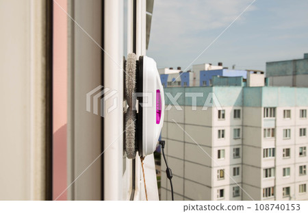 A modern vacuum robot window washer washes glass in an apartment on a balcony. View outside from the street. Safety from falls from a height. 108740153