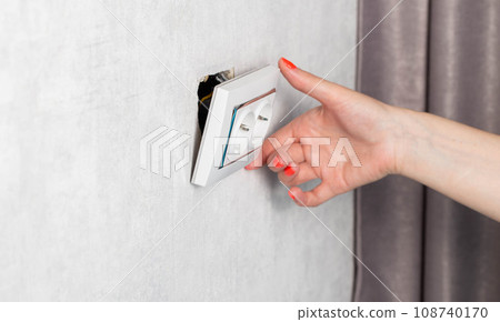 The girl is trying to insert a torn out socket from the socket due to the wrong pulling out of the electrical plug. Close-up, girl's hands with manicure. The girl is trying to insert a torn out socket from the socket due to the wrong pulling out of the electrical plug. Close-up, girl's hands with manicure. 108740170