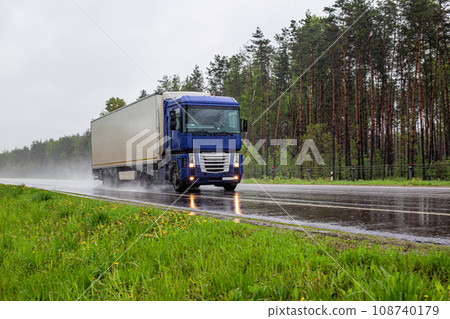 A truck with a semi-trailer transports cargo in summer in rainy weather against the background of a forest. Import and export of goods. Trucking business. Copy space for text, industry 108740179