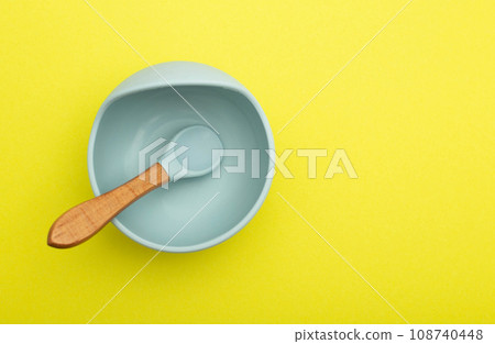 Children's blue plate with a spoon on a yellow background, close-up. Baby diet and calories for breakfast, lunch and dinner. Copy space for text. Daily calorie intake 108740448