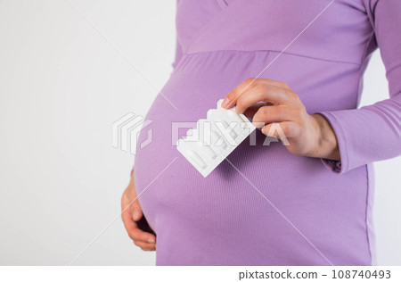 A pregnant girl in a lilac blouse holds rectal suppository against the background of her belly. The concept of treatment of constipation and hemorrhoids in pregnant women. Copy space for text A pregnant girl in a lilac blouse holds rectal suppository against the background of her belly. The concept of treatment of constipation and hemorrhoids in pregnant women. Copy space for text 108740493