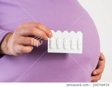 A pregnant girl in a lilac blouse holds a suppository against the background of her belly. The concept of treatment of bacterial vaginitis and rectal fissures. Close-up A pregnant girl in a lilac blouse holds a suppository against the background of her belly. The concept of treatment of bacterial vaginitis and rectal fissures. Close-up 108740678