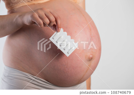 A pregnant girl holds vaginal suppositories against the background of her belly. The concept of therapeutic suppositories for genital tract infections, anti-inflammatory. Treatment of cytomegalovirus 108740679