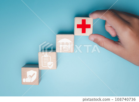 Health insurance and healthcare concept, human hand holds wooden block with icons about health insurance and healthcare access, retirement planning on blue background. Health insurance and healthcare concept, human hand holds wooden block with icons about health insurance and healthcare access, retirement planning on blue background. 108740736