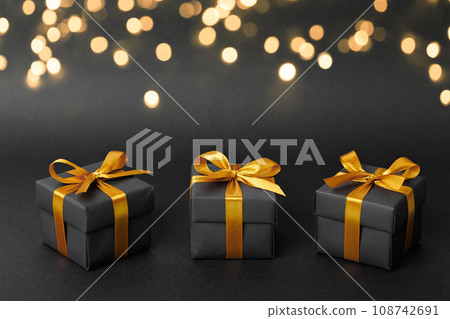 Black gift box with golden ribbon bow on black background Black gift box with golden ribbon bow on black background 108742691