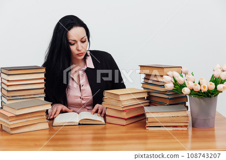 a woman in the library sits and reads a book at a table near a stack of books a woman in the library sits and reads a book at a table near a stack of books 108743207