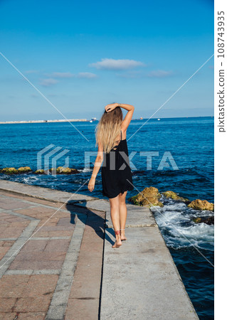 a woman walks along a pier near the sea walking the beach 108743935