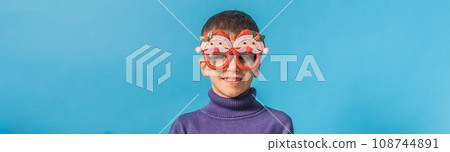 Banner Cute little child boy in party Christmas Santa Claus glasses on blue background. Kid with snow on head copy space and mockup Banner Cute little child boy in party Christmas Santa Claus glasses on blue background. Kid with snow on head copy space and mockup 108744891