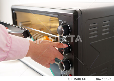 Woman's hands taking buscuit cupcakes out of mini oven 108744892