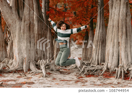 Lifestyle portrait of jumping woman in autumnal park. Stylish woman with emotions Lifestyle portrait of jumping woman in autumnal park. Stylish woman with emotions 108744954