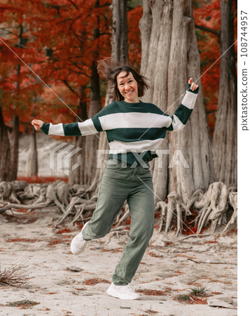 Lifestyle portrait of jumping woman in autumnal park. Stylish woman with emotions Lifestyle portrait of jumping woman in autumnal park. Stylish woman with emotions 108744957