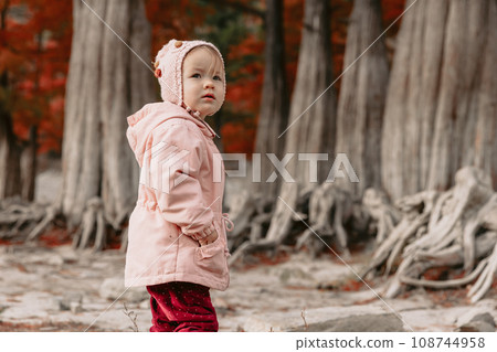 Child girl walking in a autumnal park. Little girl in warm clothes walking in the park Child girl walking in a autumnal park. Little girl in warm clothes walking in the park 108744958