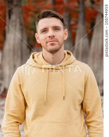 Handsome man looking at camera in autumnal forest. Caucasian young man in hoodies Handsome man looking at camera in autumnal forest. Caucasian young man in hoodies 108744959