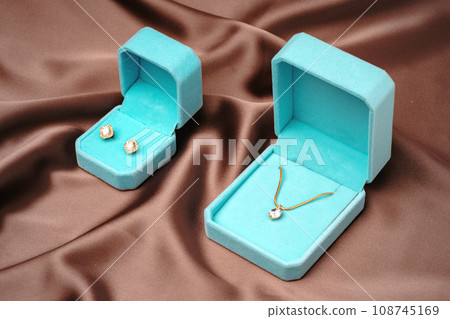 Golden necklace and earrings in blue jewelry boxes on brown silk background Golden necklace and earrings in blue jewelry boxes on brown silk background 108745169