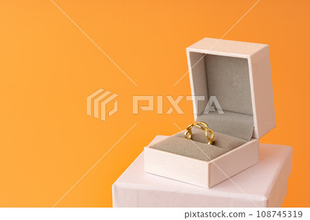 Golden ring in white jewelry box on yellow background Golden ring in white jewelry box on yellow background 108745319