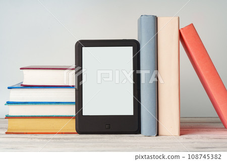 Digital tablet with a stack of books on gray background Digital tablet with a stack of books on gray background 108745382