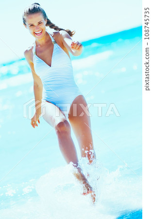 Happy young woman playing with water at seaside 108745735
