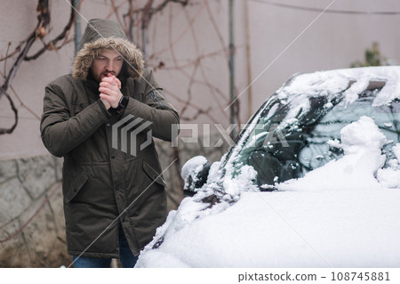 Handsome man clean his car from snow using hands. Winter outdoors Handsome man clean his car from snow using hands. Winter outdoors 108745881