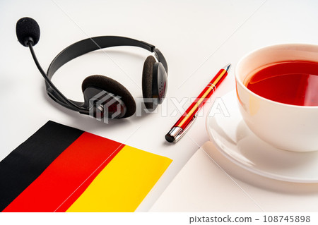 Notepad with German flag and headphones on white background. German language audio courses educational concept Notepad with German flag and headphones on white background. German language audio courses educational concept 108745898