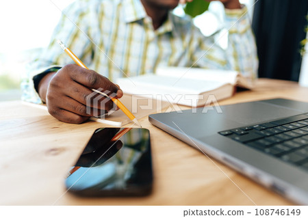 Close up photo of african businessman making notes while sitting at the table in office Close up photo of african businessman making notes while sitting at the table in office 108746149