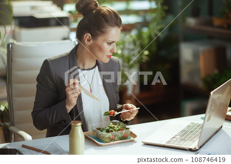 modern accountant woman in modern green office eating salad modern accountant woman in modern green office eating salad 108746419