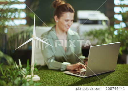 Smiling business woman in green office working on laptop Smiling business woman in green office working on laptop 108746441