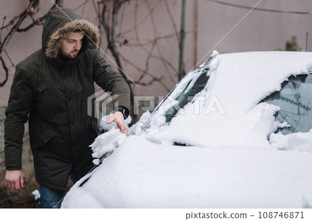 Man clean car from snow by hands after night snowfall Man clean car from snow by hands after night snowfall 108746871