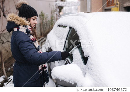 Side view of pretty female cleaning car from snow. Woman preparing for driving in the morning Side view of pretty female cleaning car from snow. Woman preparing for driving in the morning 108746872