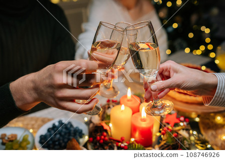 Close-up hands shot of unrecognizable happy gathering family clinking glasses with champagne, celebrating xmas, new year or birthday party, sitting at holiday dinner table with candles 108746926