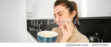 Close up portrait of happy young woman drinking coffee in the kitchen, laughing and smiling Close up portrait of happy young woman drinking coffee in the kitchen, laughing and smiling 108747993