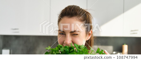 Portrait of beautiful woman cooking, holding fresh parsley, adding herbs while making salad, healthy meal in the kitchen Portrait of beautiful woman cooking, holding fresh parsley, adding herbs while making salad, healthy meal in the kitchen 108747994
