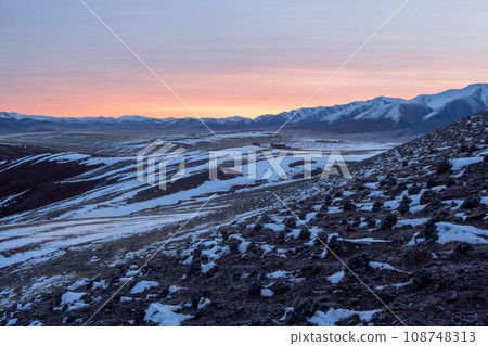 Soft pink light glides over the snow-capped peaks of the mountain 108748313