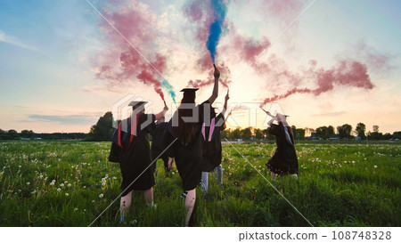 Graduates in costume walk with a smoky multi-colored smoke at sunset 108748328