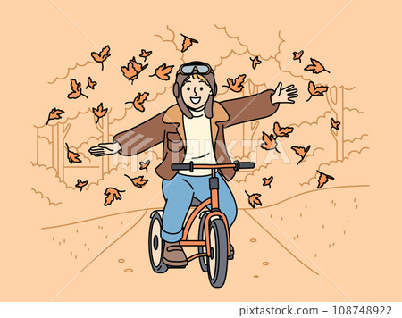 Happy child rides bicycle through autumn park and spreads arms to sides enjoying falling leaves 108748922
