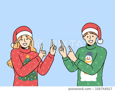 Man and woman in christmas sweaters point fingers upward to visit new year sale. 108748927