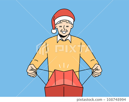 Elderly man in santa claus hat opens package with christmas gift and joy at receiving present Elderly man in santa claus hat opens package with christmas gift and joy at receiving present 108748994