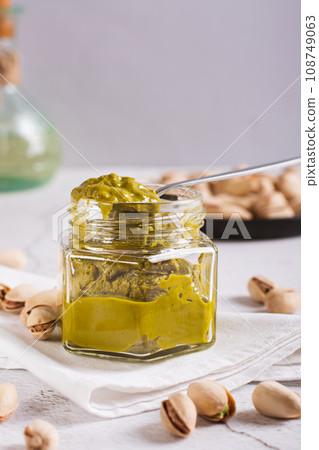 Organic pistachio spread cream in a jar and nuts on a plate on the table vertical view 108749063