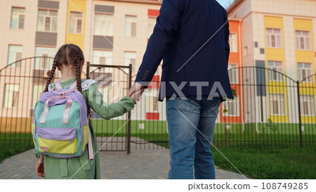 Dad accompanies little Chili with a backpack to school. Hold child's hand. Happy family. A little daughter is going to school. Children's education. The school program of children's education. Kid 108749285