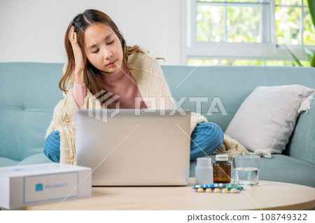 Sick young business woman sit on sofa suffering from cold covered blanket still work with laptop computer, influenza symptoms, Unwell female working online feeling sick unhealthy, medicine on desk 108749322