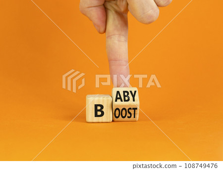 Baby boost symbol. Businessman turns a wooden cube and changes the word 'boost' to 'baby'. Beautiful orange background. Baby boost and business concept. Copy space. Baby boost symbol. Businessman turns a wooden cube and changes the word 'boost' to 'baby'. Beautiful orange background. Baby boost and business concept. Copy space. 108749476