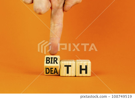 Birth or death symbol. Businessman turns wooden cubes and changes the word Death to Birth. Beautiful orange table orange background, copy space. Business and birth or death concept. 108749519